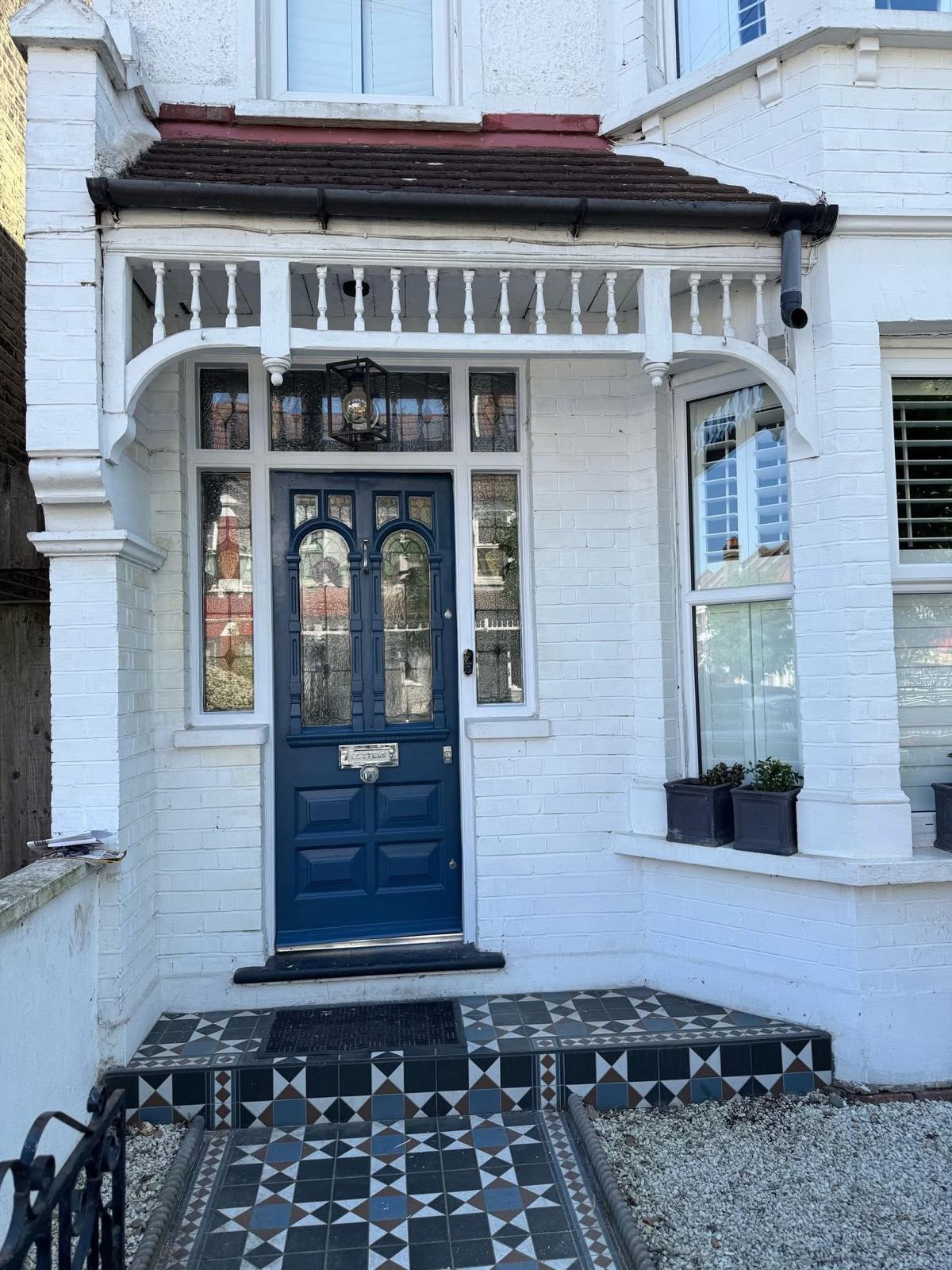 A restored Edwardian front door with arched stained-glass panels, finished in navy blue, under a turned-spindle porch with a tiled path