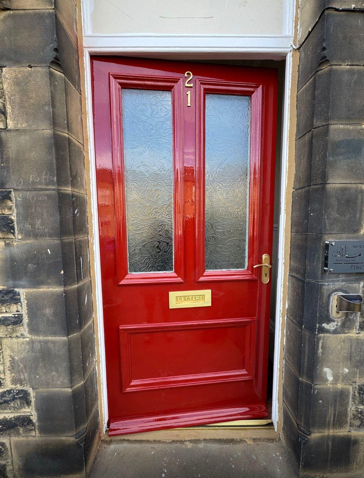 A Victorian stained-glass front door restored and finished in gloss red, with a polished brass letterplate, set in a Yorkshire stone surround